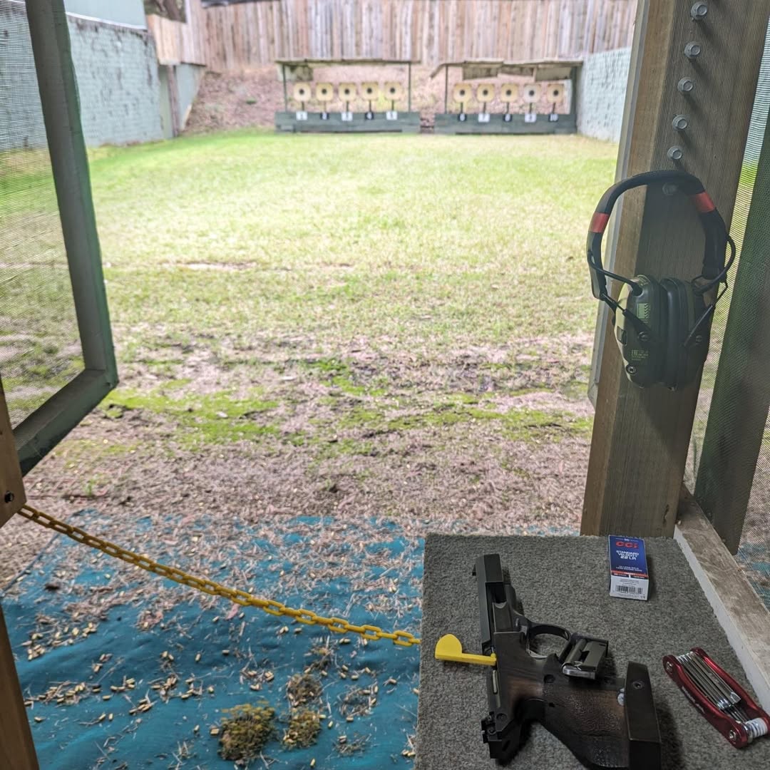 Outdoor range with a pistol on the bench and ear protection hanging nearby