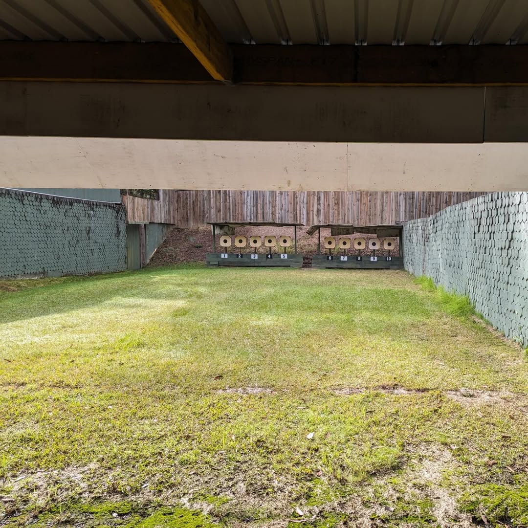 Grassy outdoor range framed by shelters and retaining walls